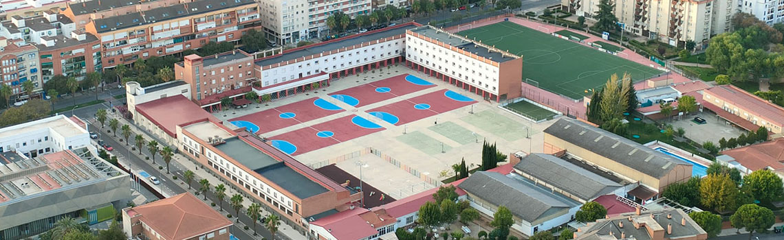 An aerial view of a school campus with buildings, basketball courts, and a soccer field in a residential area. 